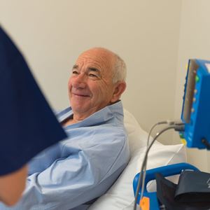 An elderly patient smiles from a bed