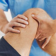 A doctor examines a knee with his hands